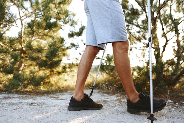 Foto mannelijke benen in comfortabele wandelschoenen met noordelijke wandelstokken op een bospad