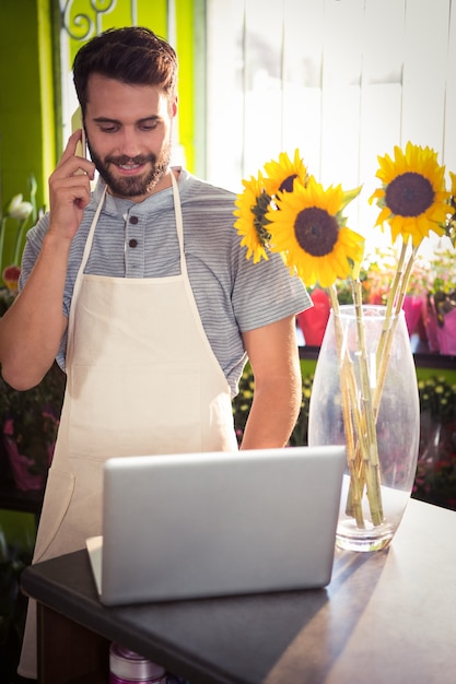 Mannelijke bloemist die op mobiele telefoon spreekt terwijl het gebruiken van laptop