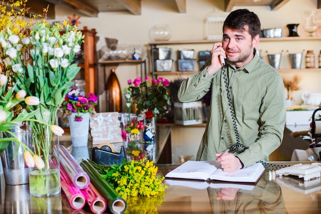 Mannelijke bloemist die orden over een telefoon in een bloemenwinkel goedkeuren