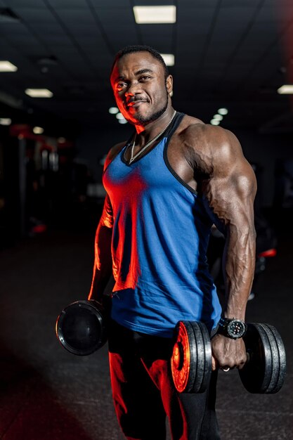 Mannelijke bodybuilder uit te werken met een zware halter. Moderne sportschool achtergrond. Blauw shirt.