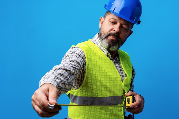 Foto mannelijke bouwer die roulette meet tegen blauwe achtergrond