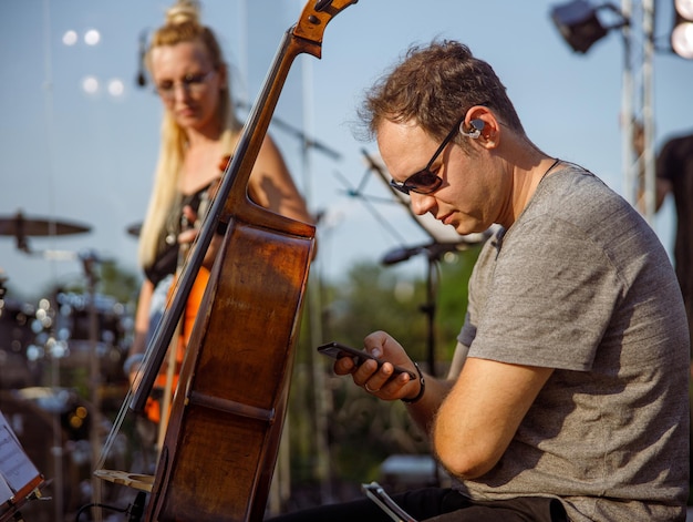 Mannelijke cellospeler die mobiele telefoon gebruikt tijdens repetitie buitenshuis
