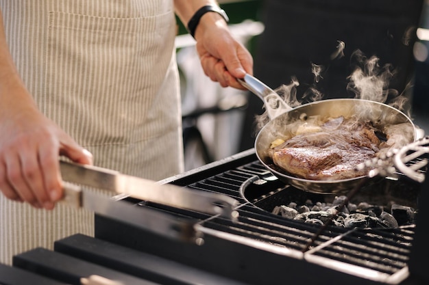 Mannelijke chef-kok bereidt tbone steak op koolstofstalen koekenpan buiten op grill bbq concept close-up