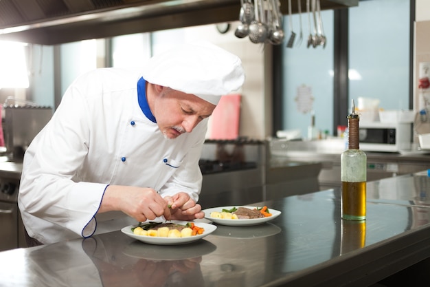 Mannelijke chef-kok gekleed in witte eenvormig decorerend een schotel