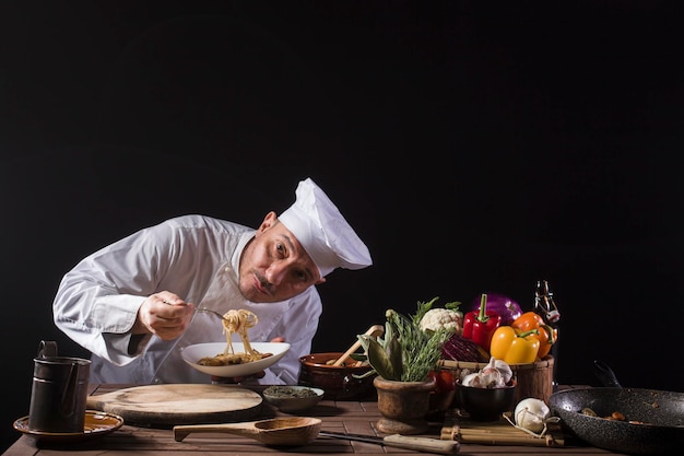 Mannelijke chef-kok in een restaurantkeuken met witte, uniform smakende spaghetti met verse groenten