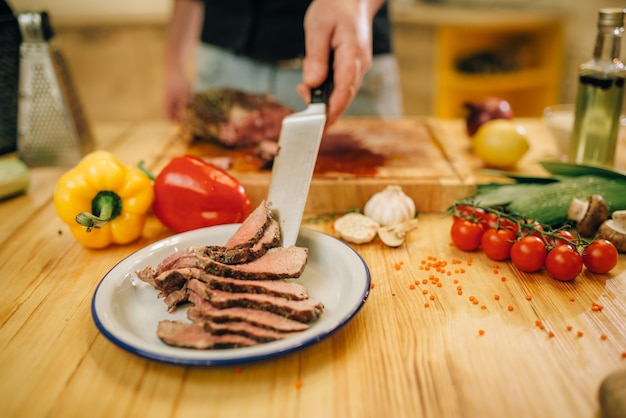 Mannelijke chef-kok met mes zet plakjes geroosterd vlees in de plaat