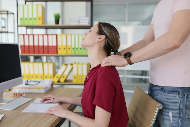Mannelijke collega masseert nek van vermoeide vrouw met sterke handen vrouwelijke werknemer in rode blouse