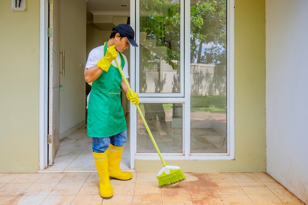 Mannelijke conciërge maakt vuile terrasvloer schoon met een bezem