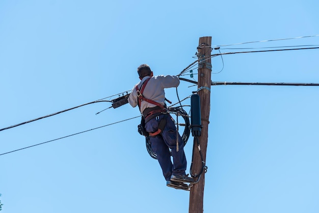 Mannelijke elektricien die stadsdraden hoog boven de stad op een ladder met harnas bevestigt