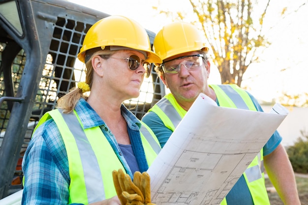 Foto mannelijke en vrouwelijke arbeiders met technische blauwdrukken praten op de bouwplaats