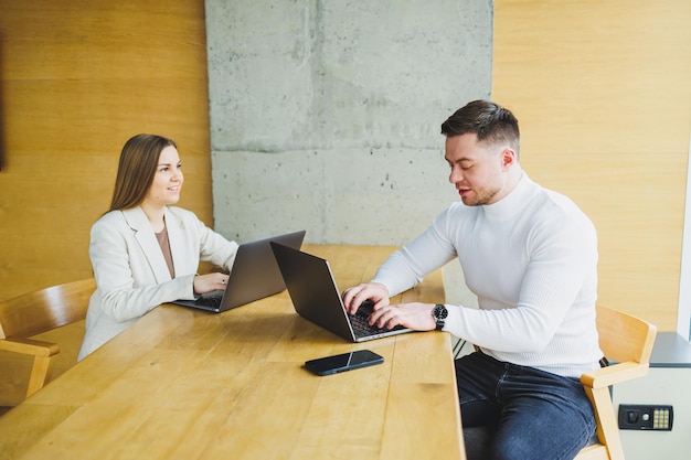 Mannelijke en vrouwelijke collega's werken aan een houten tafel op laptops en praten Concept van zakelijke samenwerking en teamwerk Jonge collega's op kantoor Moderne succesvolle mensen