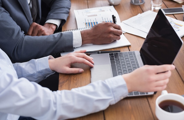 Mannelijke en vrouwelijke handen werken met laptop en zakelijke documenten tijdens meeting