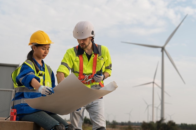 Mannelijke en vrouwelijke ingenieurs hebben een blauwdruk en bespreken het onderhoud van de windturbine in het windpark