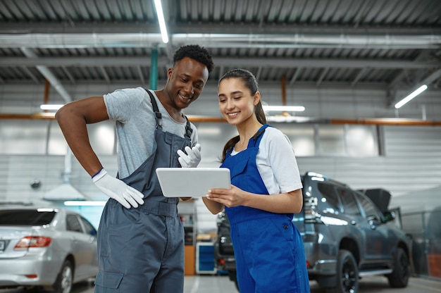 Mannelijke en vrouwelijke monteurs inspecteert motor, autoservice. Auto reparatie garage, mannen in uniform, auto station interieur. Professionele automatische diagnose