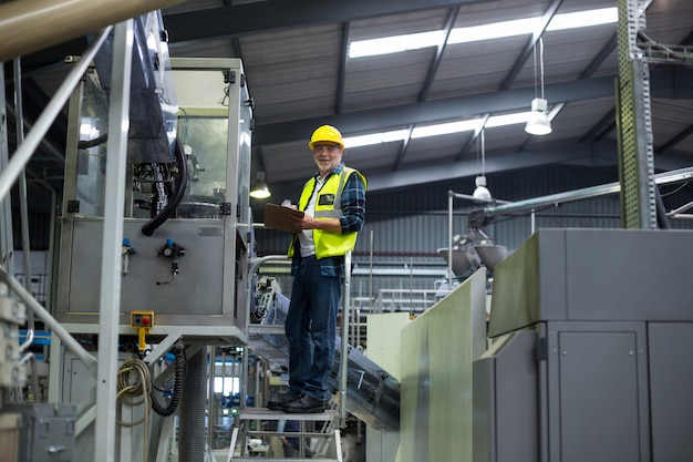 Mannelijke fabrieksarbeider die verslag op klembord handhaaft