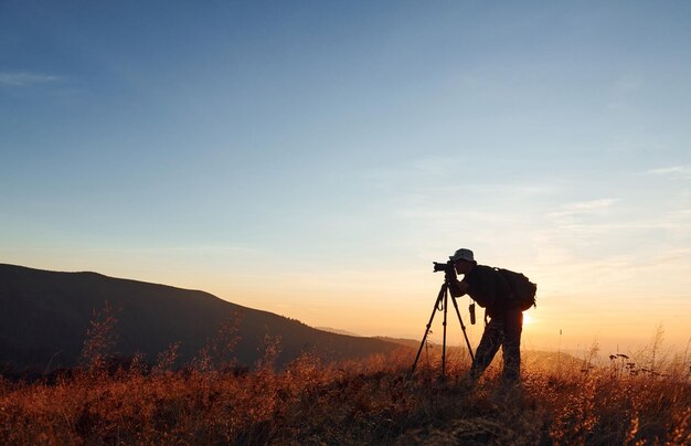 Mannelijke fotograaf staat en werkt aan een majestueus landschap van herfstbomen en bergen aan de horizon