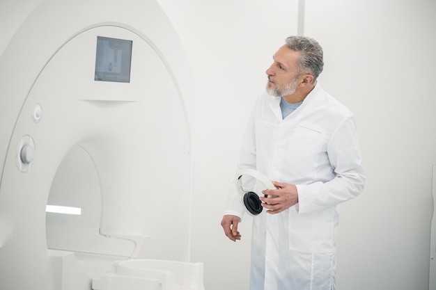 Mannelijke grijsharige arts in een laboratoriumjas in de buurt van MRI-scanner