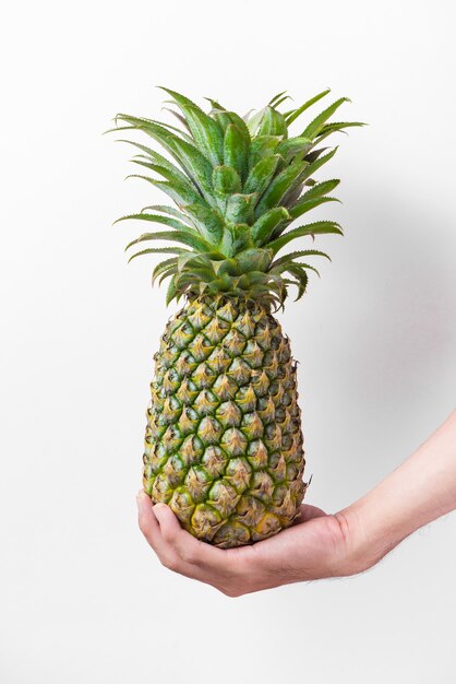 Mannelijke hand die een ananas houdt die op wit wordt geïsoleerd.