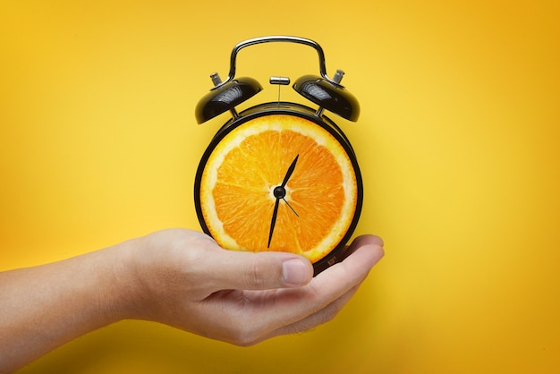 Mannelijke Hand die Wekker van Oranje Fruit op Gele Achtergrond houdt