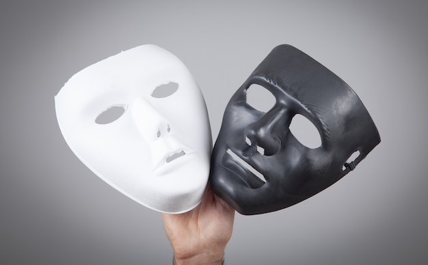 Mannelijke hand die wit en zwart masker houdt. Nep, anoniem