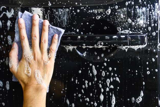 Mannelijke hand met blauwe doek die een auto wassen