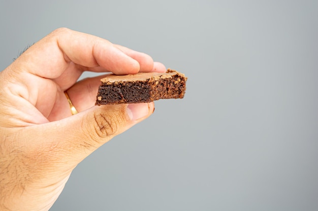 Mannelijke hand met gebeten chocolade brownie op grijze achtergrond