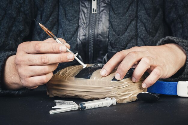 Mannelijke hand met in de palm van een plastic zak met poeder cocaïne of andere drugs en een spuit op een zwarte achtergrond