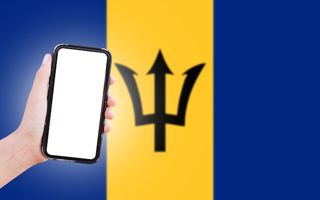 Mannelijke hand met smartphone met blanco scherm op de achtergrond van wazige vlag van Barbados Close-upweergave