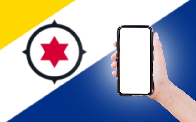 Mannelijke hand met smartphone met blanco scherm op de achtergrond van wazige vlag van Bonaire close-upweergave