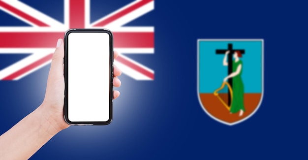 Mannelijke hand met smartphone met blanco scherm op de achtergrond van wazige vlag van Montserrat Close-upweergave