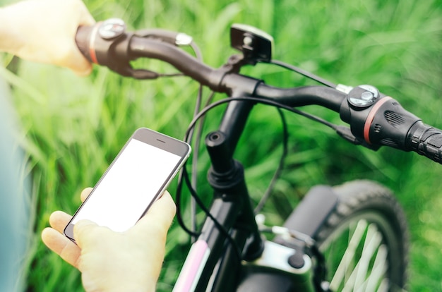 Mannelijke handen die een smartphone houden terwijl het zitten op een bergfiets op een bosweg.