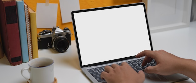 Mannelijke handen die op laptop boven huisbureau typen met camera, koffiekop, boeken en decoratie