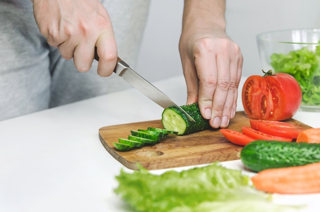 Mannelijke handen die salade voorbereiden. Komkommer snijden.