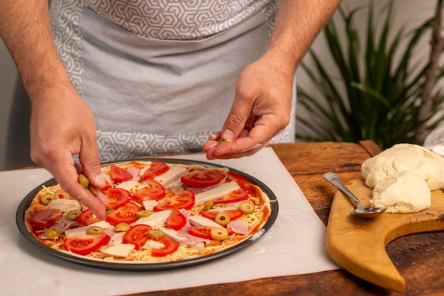 mannelijke handen die voedsel op pizza zetten