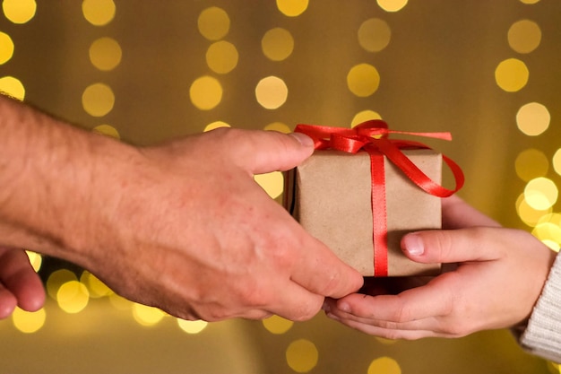 Mannelijke handen geven een kerstcadeaudoos in inpakpapier met rode strik aan de handen van het kindmeisje.