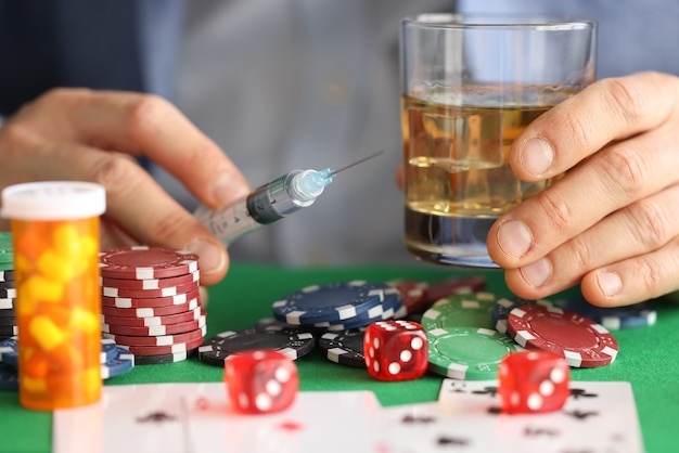 Mannelijke handen houden spuit met naald en glas met alcohol naast casinofiches