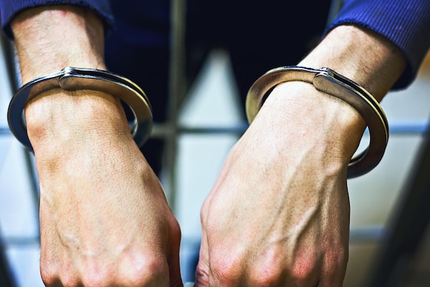 Mannelijke handen in metalen handboeien close-up een gevangene in de gevangenis het concept van straf voor een misdaad getinte afbeelding