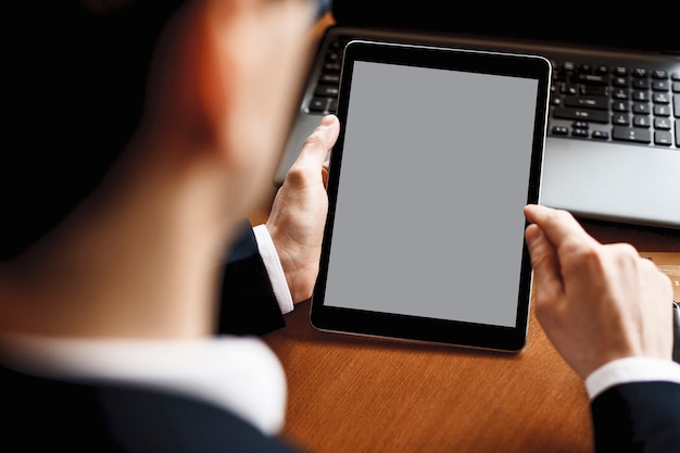 Mannelijke handen met behulp van een tablet zittend aan een bureau met een laptop erop.