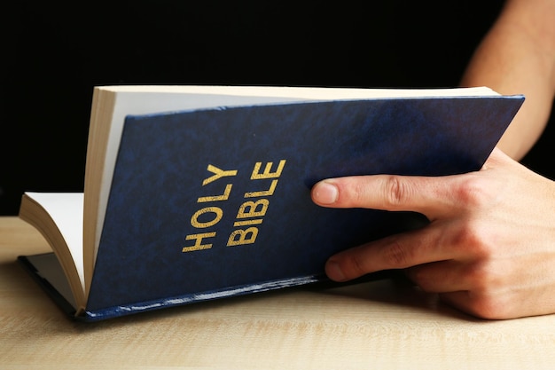 Mannelijke handen met Bijbel op houten tafel op donkere achtergrond