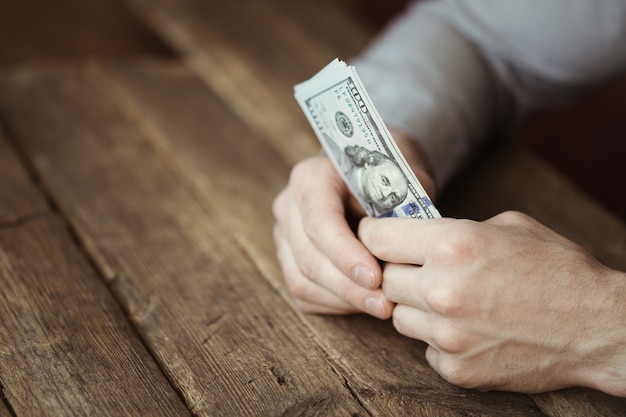 Mannelijke handen met dollar biljet op oude houten tafel