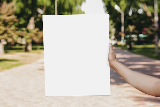 Mannelijke handen met een witte lege poster op de achtergrond van het park