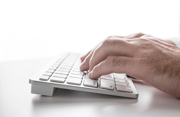 Mannelijke handen op een wit toetsenbord op een wit