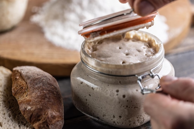 Mannelijke handen openen een pot met actief gistmeel en vers brood en gebak op de achtergrond