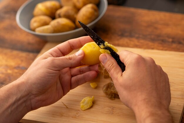 mannelijke handen schillen gekookte aardappelen over een houten oppervlak