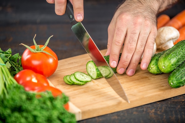 Mannelijke handen snijden groenten voor salade