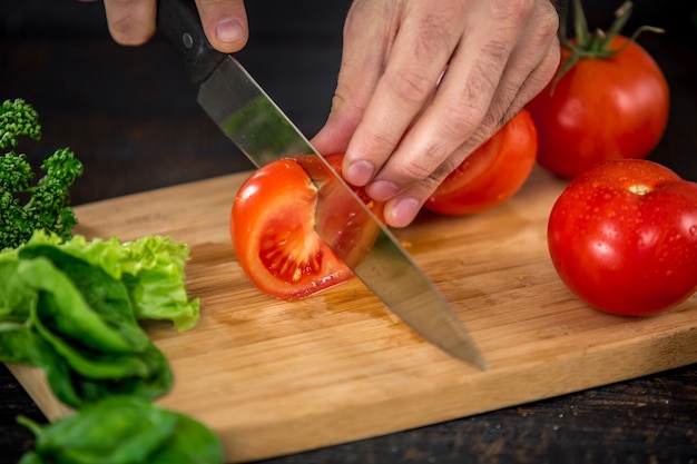 Mannelijke handen snijden groenten voor salade