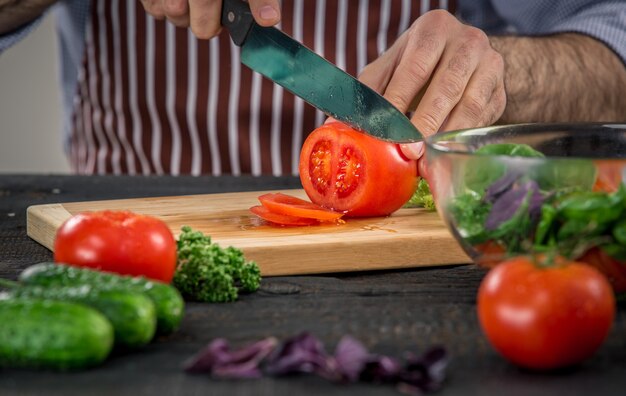 Mannelijke handen snijden groenten voor salade