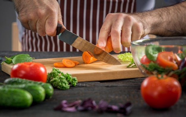 Mannelijke handen snijden groenten voor salade