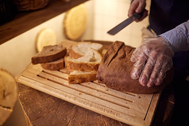 Mannelijke handen snijden tarwebrood op de houten plank, selectieve aandacht.