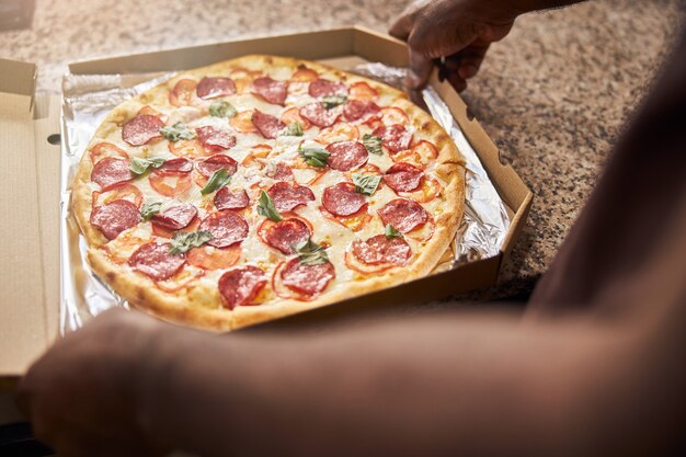 mannelijke handen verpakken heerlijke pepperoni pizza in bezorgdoos